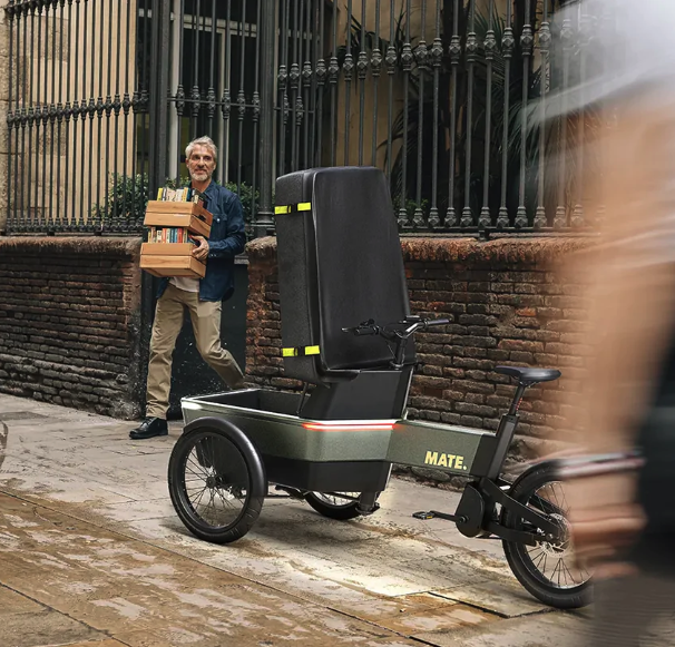 MATE SUV Cargobike Der MATE SUV wurde als perfekte Alternative zum Auto entwickelt, mit der Sie sich problemlos durch die Stadt bewegen und den Verkehr umgehen können. Ob Sie mit Ihren Kindern auf dem täglichen Schulweg, Ihrem Partner oder einem Freund unterwegs sind, auf den MATE SUV können Sie sich im Alltag verlassen. Mit einer Akkuladung legt der MATE SUV bis zu 100 km zurück und bewältigt auch schwere Lasten mit Leichtigkeit. Der starke Mittelmotor mit Tretunterstützung ermöglicht ein müheloses und bequemes Manövrieren. Mit der optionalen Regenschutzhaube müssen Sie auch an Regentagen nicht nach dem Autoschlüssel greifen und können Ihre Waren sicher ausliefern. Der MATE SUV mit seinem modularen Design und einer Reihe von Optionen bietet Ihnen die Freiheit, jede Version von Ihnen zu entdecken. Eine Auswahl an Kasteninterieur, das Allwetterdach, die Geländereifen und die exklusive MATE Wing-Technologie machen ihn zum vielseitigsten SUV auf dem Markt.
